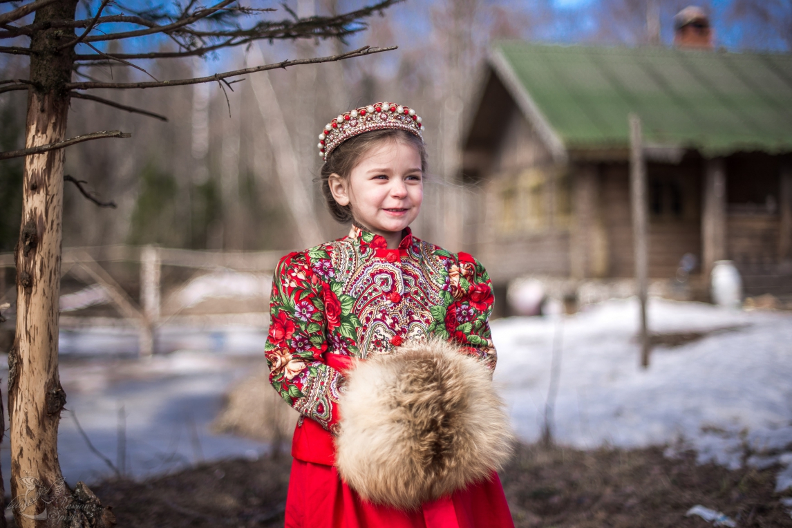 Девочка в платье в русском стиле на фоне деревянного дома