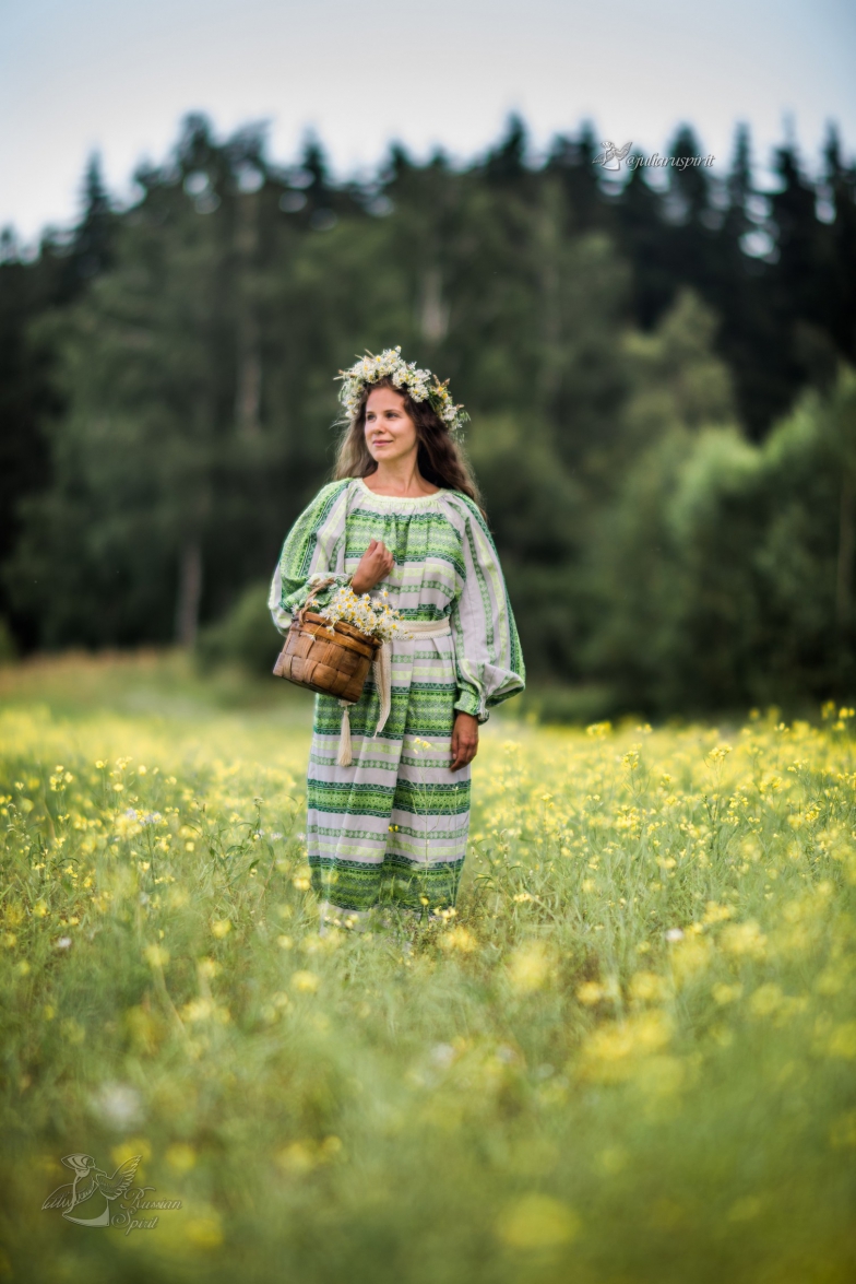 Девочка в национальном русском платье и венке в поле с корзиной ромашек